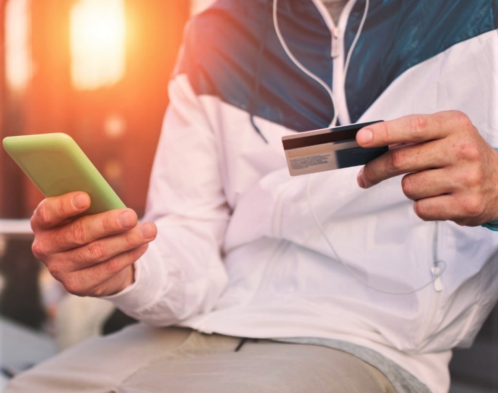 mężczyzna z telefonem oraz kartą kredytową w ręku