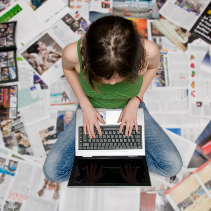 Praca na laptopie przez dziewczynę siedzącą na gazetach